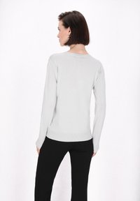 Maglione grigio chiaro a maniche lunghe con texture a coste e scollo rotondo, abbinato a pantaloni neri, visto da dietro.