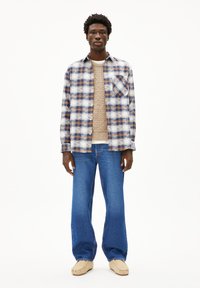 Gekruiste blouse in blauw, wit en bruin over een beige gebreide trui; gecombineerd met lichtblauwe rechte jeans en beige loafers.
