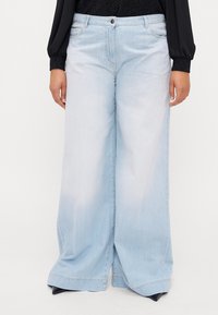 Lyseblå, vide denimbukser med en falmet vask. Har frontlommer, knappestolpe og sydd kanter for holdbarhet.