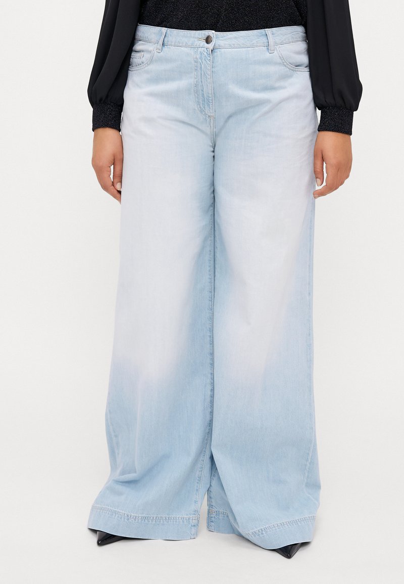 Lyseblå, vide denimbukser med en falmet vask. Har frontlommer, knappestolpe og sydd kanter for holdbarhet.