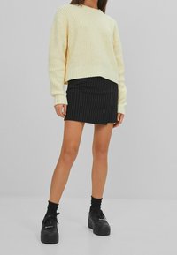 Żółty sweter z dzianiny o luźnym kroju, zestawiony z czarną mini spódnicą w prążki. Całość uzupełniają czarne sneakersy na platformie.