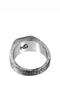 Silverring med en strukturerad, ojämn yta. Platt topp med vinklade kanter, polerad innerslang och ingraverad logotypdetalj på insidan.