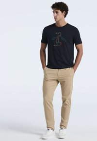 Marineblauwe t-shirt met korte mouwen dat een kleurrijk pinguïnmotief toont. Combinatie met khaki broek en witte sneakers. Soepele stof en een ontspannen pasvorm.