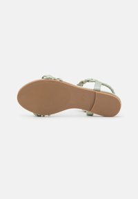 Lys grønn sandal med flettede remmer, flat såle og teksturert gummibunn. Størrelsesmærke synlig nær hælen.