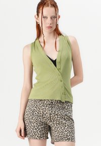 Green ribbed sleeveless top with a v-neck and button closure, paired with beige shorts featuring a black leopard print pattern.