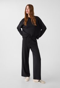 Sweatshirt noir oversize avec un col rond et des manches longues, associé à un pantalon noir large avec une taille élastiquée.