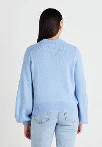 Lys blå genser med en myk tekstur, ribbede mansjetter og kant. Har klassisk rund hals og lett puffede ermer. Brukt med lyse denim.