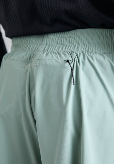 Pantalon vert menthe avec une ceinture élastique et une petite poche zippée, présentant un tissu doux et léger avec une texture lisse.