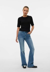 Svart ribbad kortärmad topp i kombination med ljusblå utsvängda jeans och svarta platåskor. Modellen står med ena handen på höften.