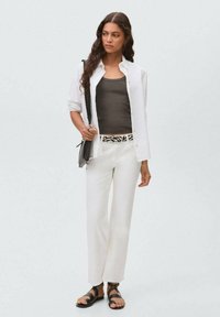White button-up shirt over a dark tank top, white trousers with a patterned belt, and black sandals. Smooth fabric with a relaxed fit.