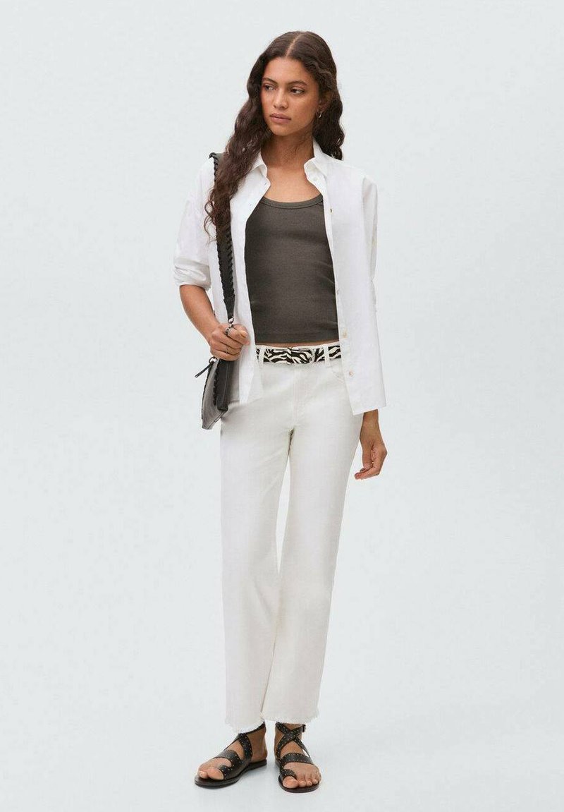 White button-up shirt over a dark tank top, white trousers with a patterned belt, and black sandals. Smooth fabric with a relaxed fit.
