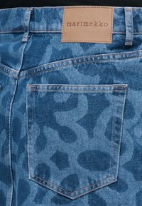 Μπλε τζιν παντελόνι με αφηρημένα σκοτεινότερα μπλε σχέδια, ορατή πίσω τσέπη και ταμπά δερμάτινη ετικέτα μάρκας με την επιγραφή "marimekko" στη μέση.