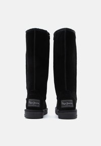 Μαύρες σουέτ μπότες μέχρι το γόνατο με αντίθετη ραφή και υφή καουτσούκ στον πάτο, διαθέτοντας ένα λογότυπο στην πίσω πλευρά.