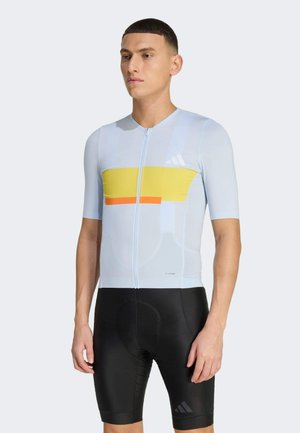 Lichtblauw fietsshirt met korte mouwen, met een gele horizontale streep en oranje accenten. Gecombineerd met zwarte, gevoerde fietsbroekjes.