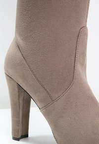 Bottine à talon haut en velours taupe avec un talon bloc et des coutures visibles sur le côté.