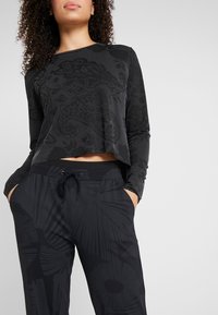 Black long-sleeve top with textured floral pattern and cropped design, paired with black pants featuring abstract patterns and adjustable drawstring.