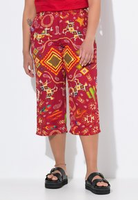 Pantaloni capri rossi con motivo geometrico e motivi animali, realizzati in tessuto leggero. Abbinati a sandali in platform neri.
