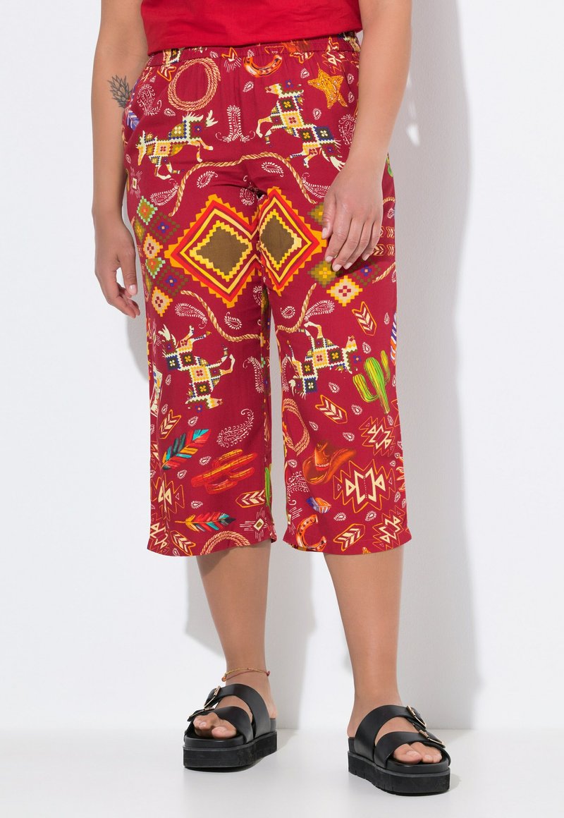 Pantaloni capri rossi con motivo geometrico e motivi animali, realizzati in tessuto leggero. Abbinati a sandali in platform neri.