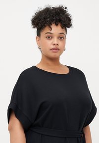 Black oversized t-shirt dress with short sleeves and a tied waist, made from soft fabric, featuring a round neckline and smooth texture.
