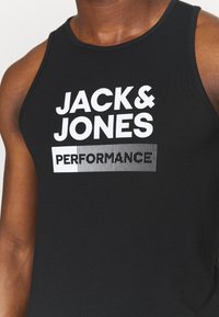 Débardeur noir sans manches avec un texte en blanc en gras "JACK & JONES" et "PERFORMANCE", accompagné d'un motif rayé en dessous.