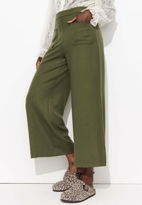 Pantalons larges vert olive taille haute, avec une poche arrière et une texture lisse. Associés à des sabots à imprimé léopard.