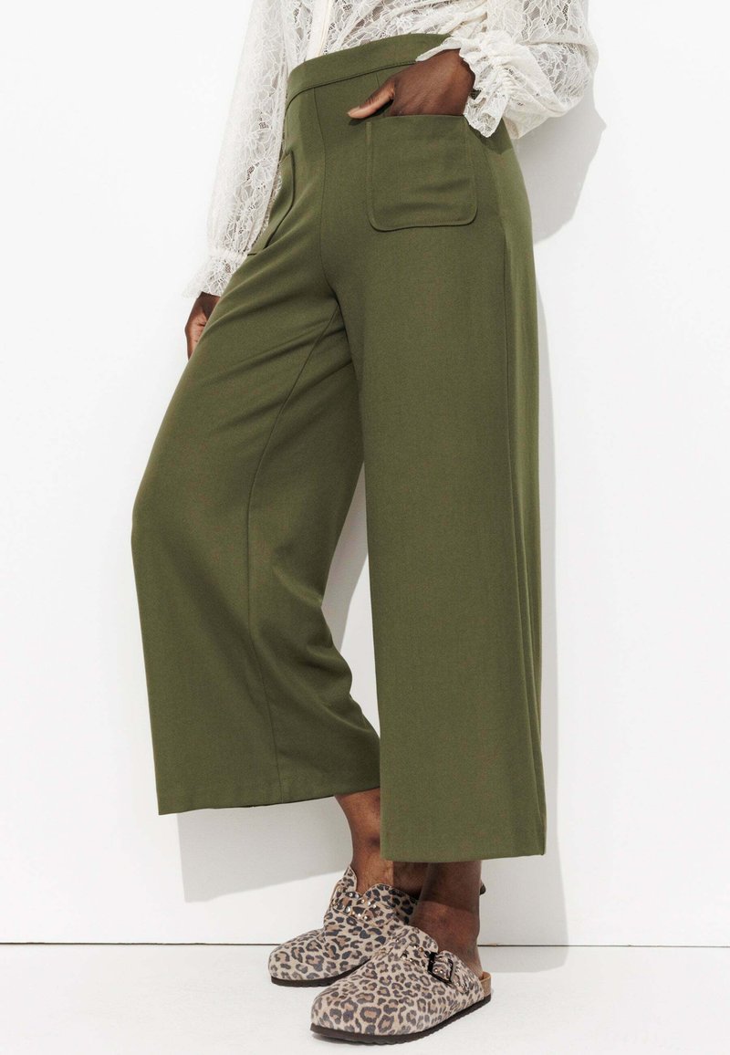 Pantalons larges vert olive taille haute, avec une poche arrière et une texture lisse. Associés à des sabots à imprimé léopard.