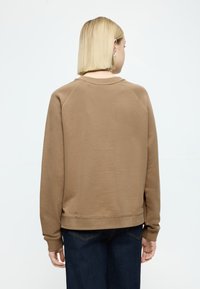 Καφέ φούτερ με ριμπ λαιμόκοψη, μακριά μανίκια και άνετη εφαρμογή. Διαθέτει λεία υφή και ραμμένη τελείωμα. Φοράται πάνω από σκούρο τζιν.