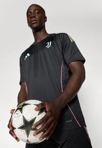 Black athletic shirt with light blue accents and pink stitching, held by a person grasping a white and black soccer ball with star patterns.