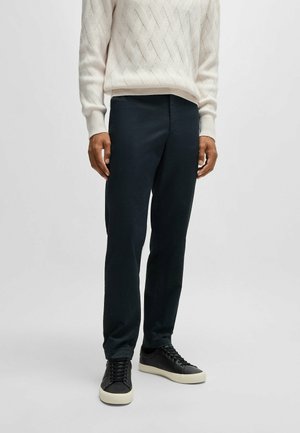 Pantaloni blu scuro con vestibilità slim, realizzati in un tessuto testurizzato. Abbinati a sneakers nere con una suola di colore chiaro.
