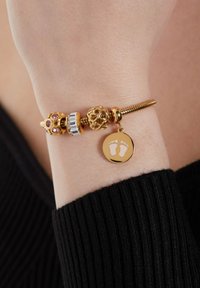Gouden armband met decoratieve bedels, waaronder een bedel met roze stenen en een ronde tag met voetafdrukken. Verstelbaar, met een textuurdesign.