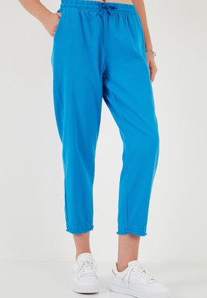 Kobieta ubrana w jasnoniebieskie krótkie spodnie z elastycznym pasem i białe trampki, stojąca na białym tle.