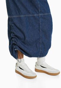 Jeans midi kjol med rynkad nederkant och justerbar dragsko, ihopparad med vita sneakers med svarta detaljer och gummisula.
