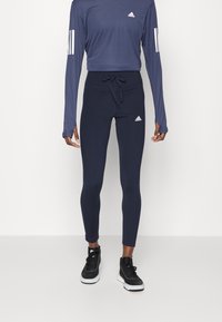 Granatowa sportowa bluzka z długim rękawem i dopasowane legginsy. Materiał wydaje się elastyczny, z trokiem w talii i białymi akcentami logo.