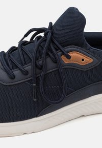 Baskets en maille marine avec un bout arrondi, une tige texturée, un accent en cuir marron et des lacets plats. Semelle en caoutchouc blanche avec un motif en vagues.