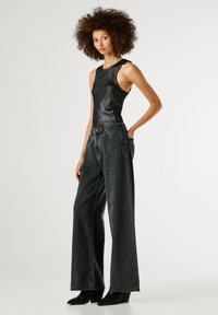 Melna mirdzoša bezpiedurkņu blūze, kas saskaņota ar plaša griezuma tumšām džinsām ar izkaisītiem rhinestones un melniem augstpapēžu zābakiem ar smailu purngalu.