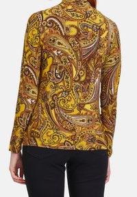 Camicia a maniche lunghe di un vivace giallo con un motivo paisley che presenta accenti marroni e neri. Tessuto morbido e design aderente.