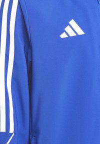 Blauwe sportjacket met een gladde textuur, voorzien van witte strepen langs de mouwen en een wit Adidas-logo aan de bovenkant.