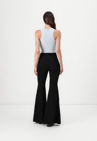 Pantaloni negri evazați cu talie înaltă, fabricați dintr-un material neted, cu buzunare la spate. Asortați cu un top din bumbac cu dungi de culoare albastru deschis.