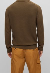 Brązowy sweter z fakturowanego dzianiny z prążkowanym kołnierzem i mankietami, w połączeniu z pomarańczowymi spodniami cargo z kieszeniami i lekko błyszczącego materiału.