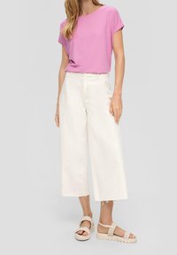 Top corto rosa a maniche corte, jeans bianchi a gamba larga con orli grezzi e sandali beige con piattaforma e cinturini intrecciati. Design pulito e moderno.