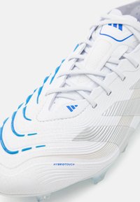 White soccer cleat with blue accents and textured patterns. Features prominent silver stripes and lace-up design, labeled "HYBRIDTOUCH."