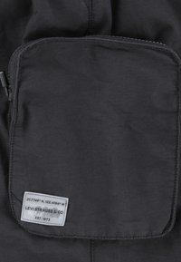 Pochette en tissu noir à texture lisse avec une fermeture éclair. Elle comporte une étiquette cousue indiquant des coordonnées et le texte "LEVI STRAUSS & CO".