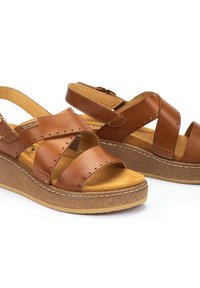 Sandales en cuir marron avec un design à brides croisées, texture granuleuse, semelle intérieure rembourrée et semelle compensée présentant une finition semblable au liège.