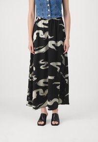 Gonna nera con un motivo beige vorticoso, realizzata in tessuto fluido; abbinata a un top corto in denim e mule neri aperti davanti.