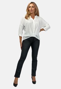 Weiße, leichte Bluse mit V-Ausschnitt und Dreiviertelärmeln, kombiniert mit schwarzen, figurbetonten Lederhosen und schwarzen High-Heels.