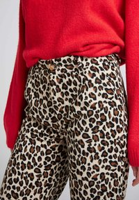 Pantalons en velours côtelé à imprimé léopard avec un fond crème et des taches noires et brunes ; dotés d'une fermeture à bouton et d'une surface texturée.