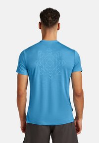 Lys blå t-shirt med korte ærmer og en glat tekstur, der har et geometrisk mønster i en lysere nuance på bagsiden.