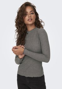 Gray long-sleeve top with ribbed texture, scalloped neckline, and fitted design. Paired with black jeans, showcasing delicate wrist details.