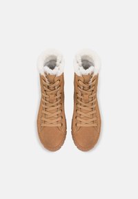 Stivali ankle in suede di colore tan con superficie tessurizzata, foderati in morbido pellicciotto sintetico bianco e dotati di lacci. La suola in gomma presenta dettagli antiscivolo.