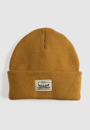 Beanie a maglia color senape con texture a coste. Presenta un risvolto e una toppa rettangolare con dettagli grafici in bianco e nero.